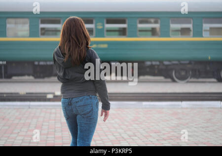 Une jeune fille aux cheveux roux est debout sur le quai de la gare et regarder le train au départ. La femme était en retard pour son train. Vue arrière Banque D'Images