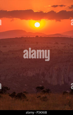 Vue Portrait d'un coucher de soleil rouge avec le soleil un bas boule blanche sous nuages orange au Blyde River Canyon cliffs à Mpumalanga, Afrique du Sud Banque D'Images