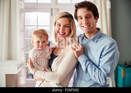 Portrait Of Smiling Family Holding Baby Daughter In Nursery Banque D'Images