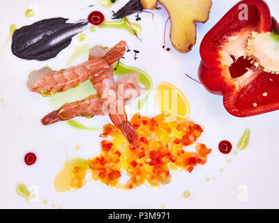 Trois crevettes sur un tableau blanc décoré avec des morceaux de légumes et sauce. Banque D'Images