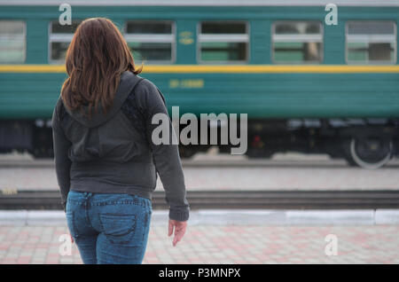 Une jeune fille aux cheveux roux est debout sur le quai de la gare et regarder le train au départ. La femme était en retard pour son train. Vue arrière Banque D'Images