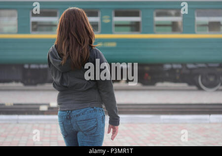 Une jeune fille aux cheveux roux est debout sur le quai de la gare et regarder le train au départ. La femme était en retard pour son train. Vue arrière Banque D'Images