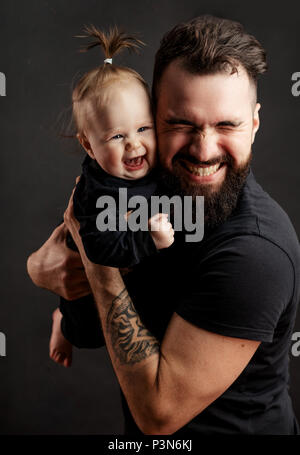 Beau jeune homme tatoué holding cute little baby sur fond noir Banque D'Images