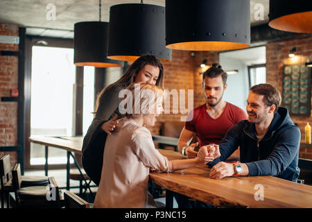 Cheerful gyu et girl having fun Arm wrestling les uns les autres dans un pub. Banque D'Images