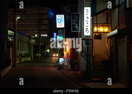 Photo de nuit de la rue vide à Aomori, Japon, avec les phares de voitures à la fin de la route et le japonais neon bannières comme la seule source de lumière. Banque D'Images