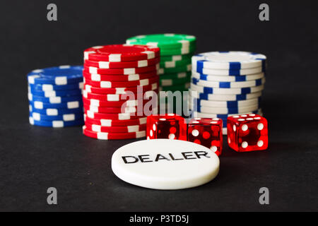 Des jetons de poker et Red Dice avec badge revendeur en premier plan et arrière-plan noir Banque D'Images