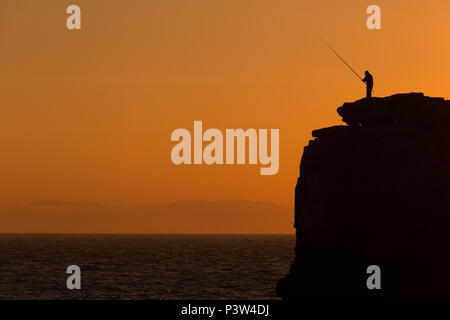 Un pêcheur se dresse au sommet d'Pulpit Rock près de Portland Bill, Dorset, au coucher du soleil. Banque D'Images