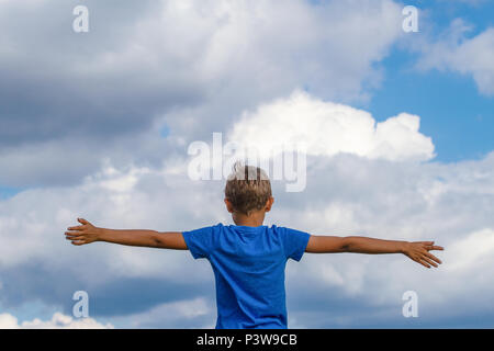 Happy kid avec bras levés contre le ciel bleu. La liberté, la joie et le bonheur concept Banque D'Images