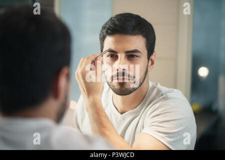 Latino Man Trimming sourcil pour les soins du corps dans la salle de bains Banque D'Images