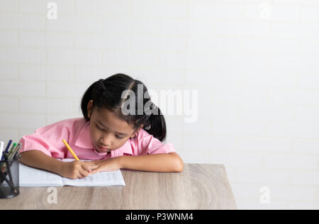 La petite fille est en train de faire ses devoirs avec attention. Les enfants utilisent un crayon jaune est l'écriture d'un ordinateur portable sur la table en bois. Sélectionnez l'accent faible profondeur de fiel Banque D'Images