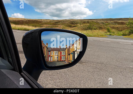 Conduire dans la campagne avec des maisons en terrasse urbaine reflète dans la voiture wing mirror. Banque D'Images