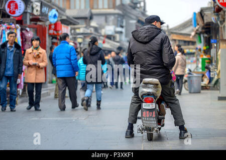 BEIJING, CHINE - le 12 mars 2016 : vélos, scooters et voitures dans les rues de Pékin. Au milieu de la rue, un homme est assis sur un scooter. Banque D'Images