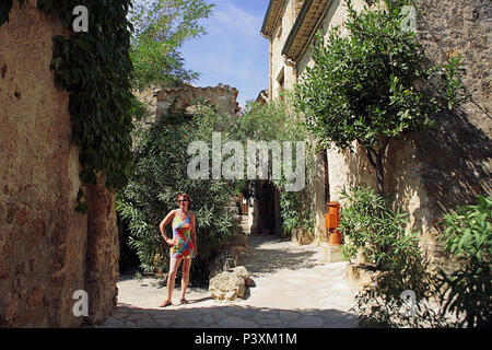 Une femme pose dans ruelle tranquille (Rue du Teron) dans le village médiéval de Saint-Guilhem-le-Désert, Hérault, Occitanie, France. Parution du modèle Banque D'Images