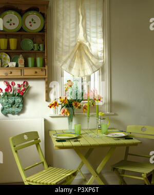 Petite table en bois pliante peint vert et chairsbelow crème avec petite fenêtre aveugle dans la salle à manger de style économie Banque D'Images