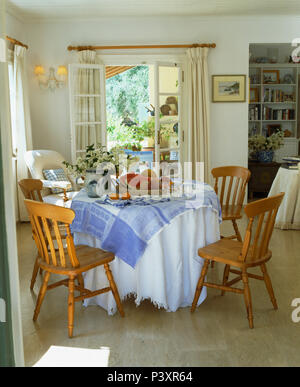 Chiffons bleu et blanc sur la table circulaire avec des chaises en bois simple côtier grec en salle à manger avec portes-fenêtres Banque D'Images