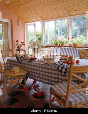 Blanc +bleu tissu vérifié sur table avec chaises en rotin dans pays simple salle à manger avec un plafond en bois en pente Banque D'Images