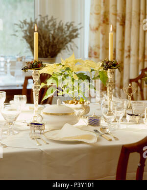 Des bougies allumées dans les chandeliers d'argent avec crème poinsettia sur set de table pour le déjeuner avec des couverts en argent et la chine antique Banque D'Images