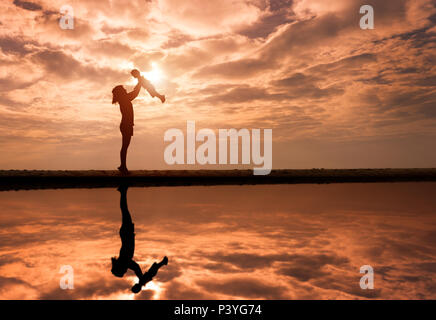 Reflet de son petit ascenseur mère Silhouette contre le coucher du soleil et reflets en mer. L'activité de la famille asiatique de vie. Banque D'Images