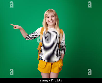 School girl smiling avec sac à dos du doigt quelque chose contre un arrière-plan vert Banque D'Images