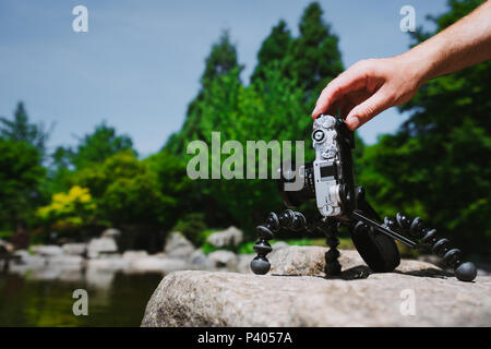 Homme Photo manipulation à la main un vieux millésime caméra sur trépied en face de l'eau étang parc Planten un Blomen à Hambourg, Allemagne Banque D'Images