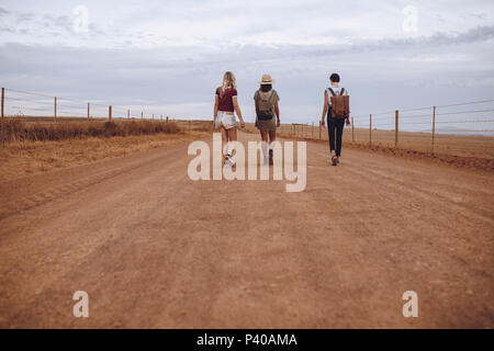Vue arrière de trois jeunes femmes marchant sur la route de campagne. Femme amis marchant sur une route rurale. Banque D'Images