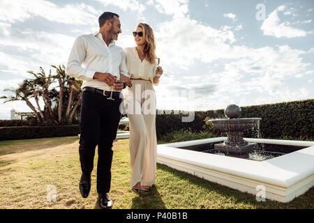 Couple élégant la marche à l'extérieur en pelouse avec un verre de vin. L'homme et de la femme à l'un l'autre et marcher ensemble à l'extérieur.. Banque D'Images