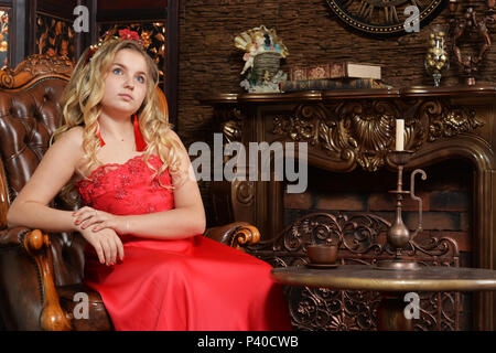 Adolescente blonde en robe rouge vif sitting in armchair Banque D'Images