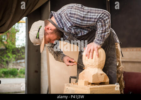 Jeune homme dans un menuisier scies vêtements de travail à la tête d'un homme avec un arbre , à l'aide d'un burin dans l'atelier, autour d'un lot d'outils pour le travail Banque D'Images