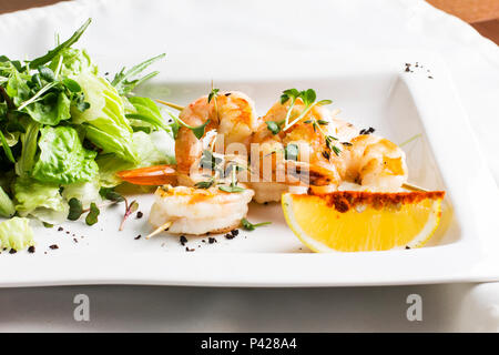 Crevettes géantes en brochettes avec du citron et des verts sur un plat blanc Banque D'Images