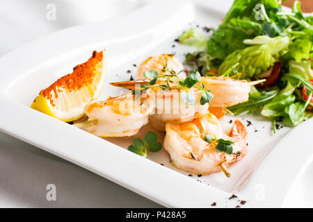 Crevettes géantes en brochettes avec du citron et des verts sur un plat blanc Banque D'Images