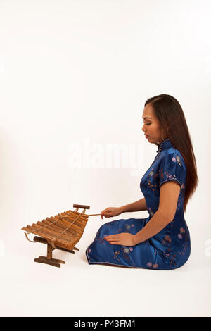 Femme chinoise jouant un xylophone de bambou avec un hérisson en bois. Instrument traditionnel. Banque D'Images