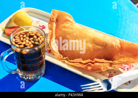 Une cuisine traditionnelle tunisienne - des pâtisseries avec de la viande ('Brik') et le thé avec les noix de pin et de menthe. Focus sélectif. Banque D'Images