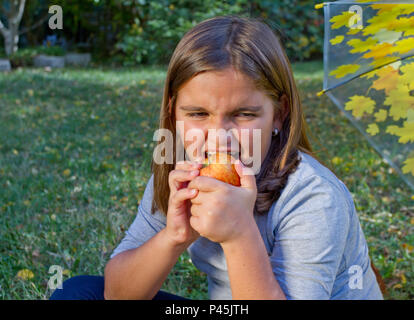 Preteen enfant manger pomme rouge avec ses dents en bonne santé et le souffle de l'air frais. Cute little girl de moustiques des fruits orange pomme sur le prêt. Closeup portrait of h Banque D'Images