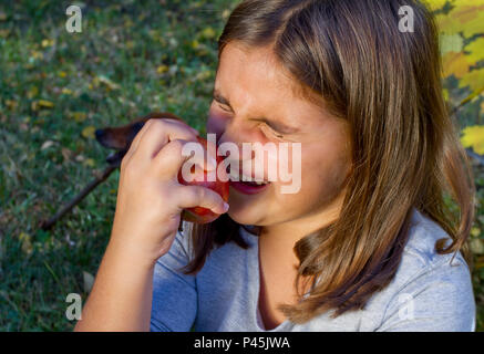 Cet enfant une pomme rouge et a un lourd de dents. Cute little girl manger des fruits orange et Apple se sentir la douleur de la dent. Closeup portrait of kid cris de toot Banque D'Images