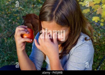 Cet enfant une pomme rouge et a un lourd de dents. Cute little girl manger des fruits orange et Apple se sentir la douleur de la dent. Closeup portrait of kid cris de toot Banque D'Images