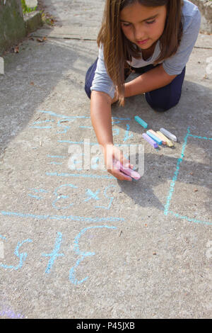 Kid Fille de réflexion, de rédaction et de compter sur des équations mathématiques avec les craies de couleur sur un trottoir. L'école et vacances. Concept de l'éducation. S Banque D'Images