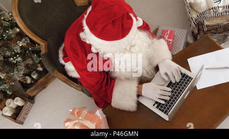 Le Père Noël chargé de dresser une liste de cadeaux sur son ordinateur portable Banque D'Images