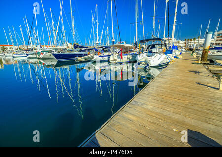 Jetée en bois avec voiliers reflétée sur mer bleue en Baie de Lagos. Paysage du port de plaisance de Lagos sur côte de l'Algarve, Portugal, Europe. Vacances d'été. Banque D'Images