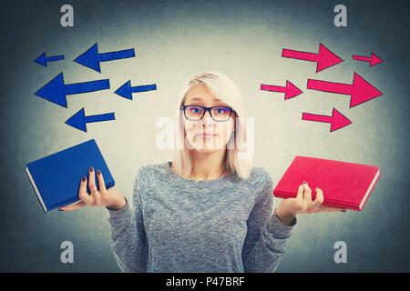 Jeune femme confuse de choisir entre deux livres, rouge et bleu, avec des flèches poinded à gauche et à droite. Décision difficile, l'éducation, concept Banque D'Images