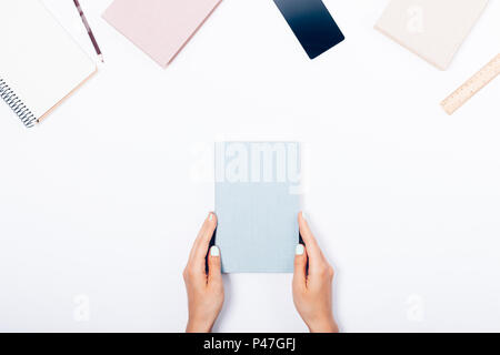Les mains tenant un livre bleu entre les ordinateurs portables, smartphones, règle et crayon, vue d'en haut. Le travail et les études stylisé 24 collage sur zone blanche Banque D'Images