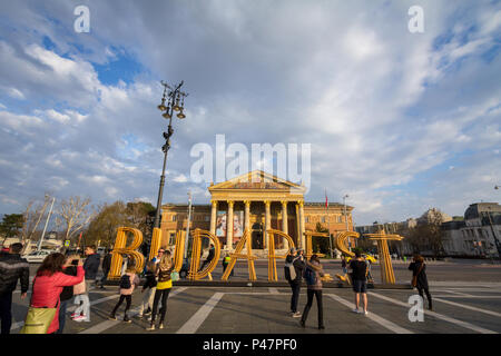 BUDAPEST, HONGRIE - le 7 avril 2017 : les touristes prenant des photos devant un signe de Budapest avec le Muscarnok (Hall of arts) en arrière-plan sur Heroes squa Banque D'Images