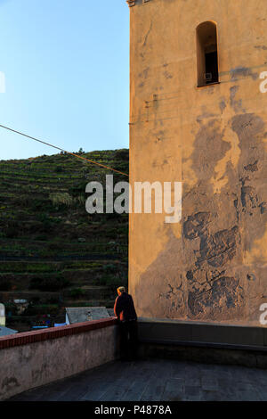 Un homme seul dans la pensée et éclairées par la lumière de la jante comme il se trouve à côté de la tour de cloche en début de soirée forte lumière, Manarola, Cinque Terre Banque D'Images