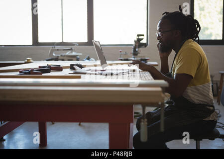 Carpenter talking on mobile phone while using laptop Banque D'Images