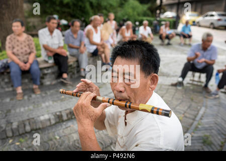 L'homme joue de la Flûte en bois traditionnel pour les adultes dans la rue de la ville et à la brunante, Ville de Nanyang, Qingdao, Shandong Province, China Banque D'Images