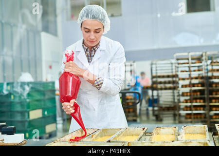 Travailleur d'usine de confiserie à l'aide de poche à pâtisserie Banque D'Images