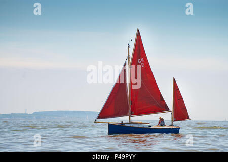 Un voilier rouge vu sur mer calme sur une chaude journée ensoleillée avec ciel bleu. Banque D'Images