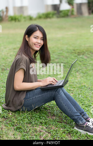 Image ado asiatique unique sourire étudiant en utilisant un ordinateur portable avec les données de l'entreprise travaillant dans l'université. Banque D'Images