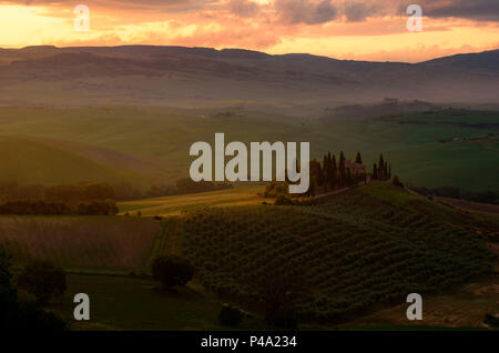 Podere Belvedere, San Quirico d'Orcia, province de Sienne, Toscane, Italie. Le lever du soleil sur la maison et les collines. Banque D'Images