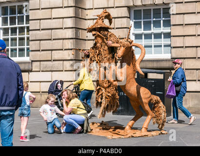 Edinburgh, Ecosse, Royaume-Uni, 21 juin 2018. Un artiste de rue dans une loi de lévitation habillé comme Gandalf l'assistant avec une licorne pour divertir les passants par sur le Royal Mile pendant la saison estivale. Une femme et des enfants sont divertis par la loi sur la rue que les gens passer Banque D'Images