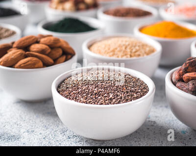 Les graines de Chia dans petit bol blanc et d'autres de l'air sur l'arrière-plan. Focus sélectif. De l'air différents ingrédients. Concept et illustration pour superfood et detox food Banque D'Images